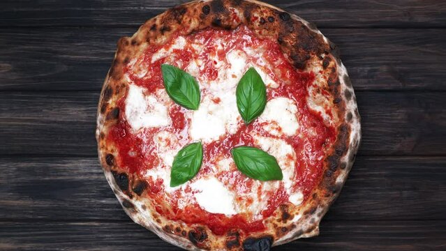 Tasty pizza Margherita with mozzarella cheese,tomatoes and fresh basil on old wooden table.Top view and rotation.Delicious Neapolitan Pizza Margherita.italian food.Restaurant Pizza Food.Italy
