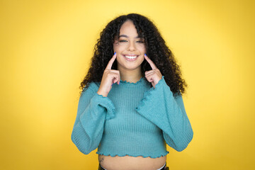 African american woman wearing casual sweater over yellow background smiling confident showing and pointing with fingers teeth and mouth