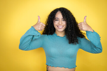 African american woman wearing casual sweater over yellow background success sign doing positive...