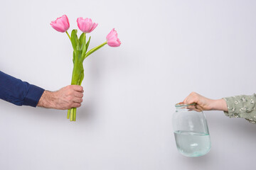 A man puts a bouquet of pink tulips in a jar of water.