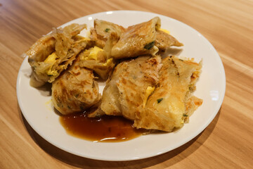 Close up of delicious Taiwanese omelette, egg pancake roll cut into pieces with ham, soy sauce on a white plate. There is copy space. The food is for breakfast