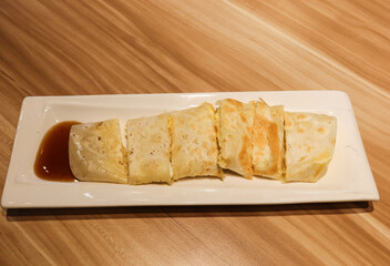 Close up of delicious Taiwanese omelette, egg pancake roll cut into pieces with ham, soy sauce on a white plate. There is copy space. The food is for breakfast