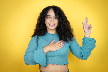 African american woman wearing casual sweater over yellow background smiling swearing with hand on...