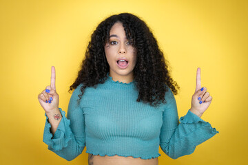 African american woman wearing casual sweater over yellow background amazed and surprised looking...