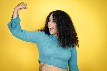 African american woman wearing casual sweater over yellow background showing arms muscles smiling...