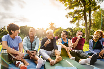 Happy multiracial senior friends drinking a tea after workout activities in a park - 766312410