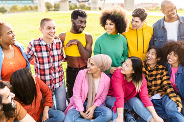 Happy young multiracial people having fun sitting on grass in a public park - Diversity and...