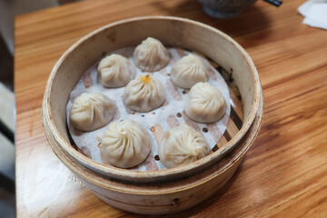 close up of Taiwanese Chinese steamed meat soup dumplings in a bamboo caged container on a wooden table