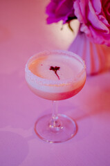 close up of a pink cocktail on a table with candles and roses