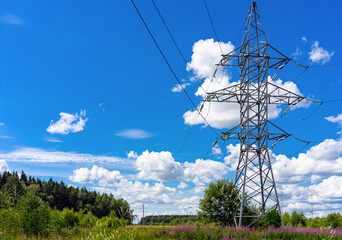 Electric high-voltage line tower power pole stands in a green field in summer day against blue sky with white clouds. Copy space
