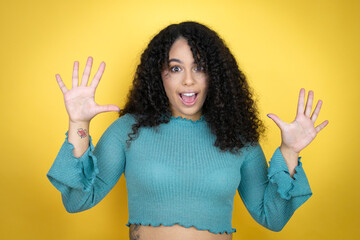 African american woman wearing casual sweater over yellow background showing and pointing up with fingers number ten while smiling confident and happy