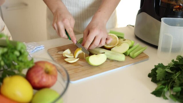 Woman making detox beverage at home. Organic products on wooden table. Female peel a lemon. Apple, kiwi, celery, and cucumber