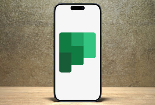 Microsoft Planner logo is displayed on a modern smartphone standing on a wooden desk, planning application available on the Microsoft 365 platform, team management, file sharing, and organization