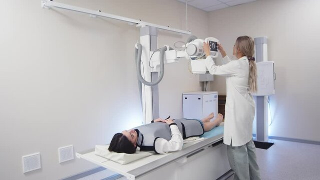 A specialist doctor in an X-ray room, a radiologist sets up a machine for radiography of a patient and makes a scan. The concept of medical technologies, modern medical equipment.