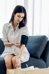 Woman measuring blood pressure by using digital sphygmomanometer at home. Woman using medical device to measure blood pressure.