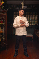 Full body photo of a young FIlipino man in traditional Barong Tagalog shirt and slacks, inside an ancestral house.