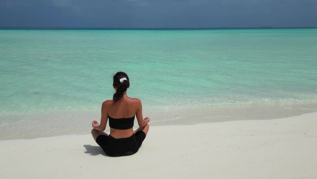 woman doing yoga practice for breathing and calming on Maldives beach aeiral view