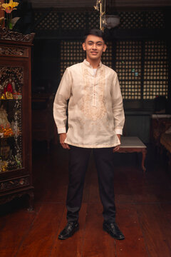 Full body photo of a young FIlipino man in traditional Barong Tagalog shirt and slacks, inside an ancestral house.
