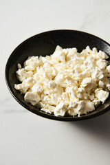 Cottage cheese in the black plate on white marble backgorund. Tasty, full of protein and healthy breakfast idea.