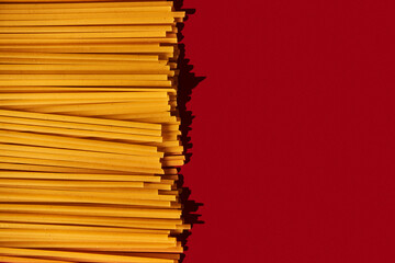Linguine raw pasta macaroni background on vibrant and contrast red backgrorund. Hard light,...