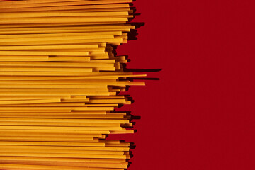 Linguine raw pasta macaroni background on vibrant and contrast red backgrorund. Hard light,...