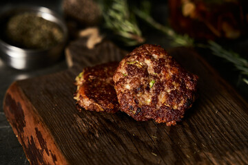 Beef, zucchini and cheddar cheese patties or cutlets on wood board. Low key food photo, dark background. Dinner meat concept, full of proteins.
