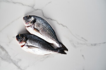 Two raw and fresh dorado fish on white marble background. Minimalistic food photo. Mediterranean diet. Top view, copyspace