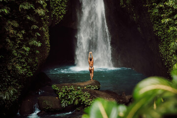 Waterfall and woman in bikini. Traveler girl posing near waterfall