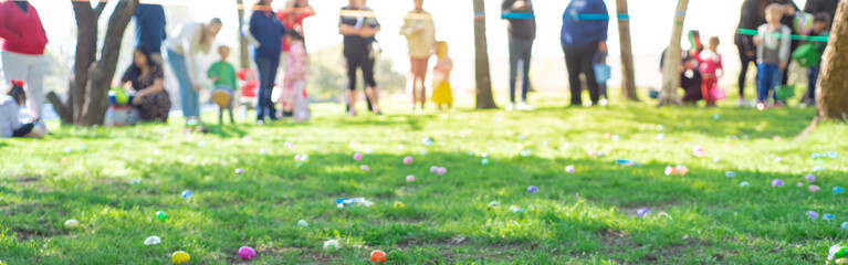 Panorama selective focus long line of diverse kids with parents after brightly colored barricade tape and multicolor Easter eggs on Church grass meadow field ready for egg hunt tradition, Texas