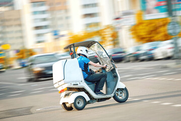 Delivery man on electric scooter deliver food. Food delivery man riding on enclosed scooter,...