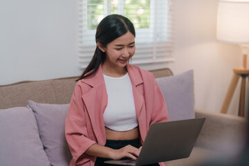 Woman in a pink jacket is sitting on a couch and using a laptop