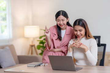 Smiling joyfully, two women share a moment of success in front of a laptop in a bright and modern home office