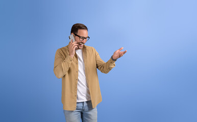 Young male freelancer laughing and discussing ideas over mobile phone on isolated blue background