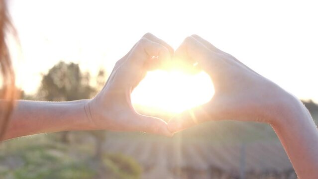 Woman making heart shape with hands against beautiful sunset concept