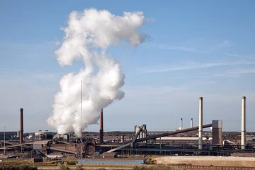 Foto auf Alu-Dibond Rokende schoorstenen door staalproductie bij Tata Steel in Ijmuiden, tegen een blauwe lucht. © ArieStormFotografie