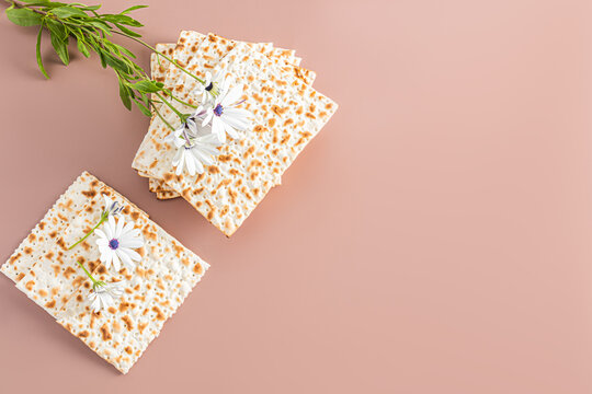 Concept of celebrating the Jewish holiday of Passover. A stack homemade matzoth on beige background and a delicate flower. Top view. a place for text.