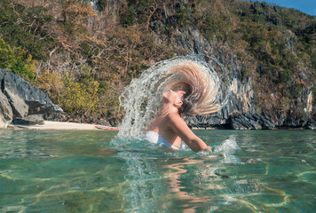 Woman Flipping Her Hair in Clear Waters Near a Rocky Cliff on a Sunny Day