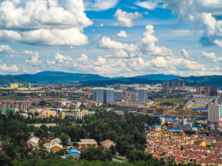 Yunan, China - June 9, 2016 : Aerial photograph of a metropolis' buildings with cloud at the blue sky in background. There were mountains all around the town.