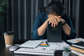 Woman with hands clasped praying while sitting at desk in office. Businesswoman praying at work....