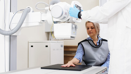 A specialist doctor in an X-ray room, a radiologist sets up a machine for radiography of a patient...