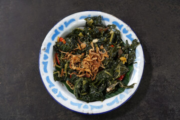 Stir-fried papaya leaves served on a classic plate on a wooden table                