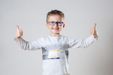 A young boy, wearing glasses, enthusiastically gives a thumbs up gesture