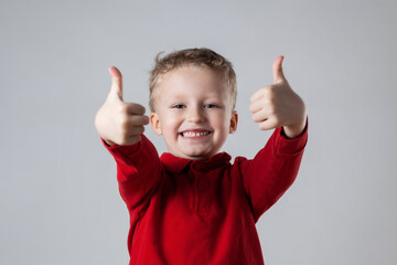 A young boy wearing a red shirt is smiling and giving a thumbs up gesture