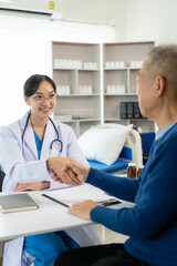 Fototapeta premium Old man shaking hands to greet a friendly Asian female doctor with a stethoscope around her neck shaking hands with a middle-aged male patient to reassure her in the hospital medical help