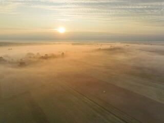 Fototapeta premium Brzask na wsi z lotu ptaka, ujęcia z drona wsi o brzasku, wschód słońca na wsi, pusząca się o poranku wieś, pola owite mgłą o brzasku, poranek we mgle