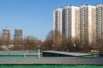 View of multi-storey panel residential buildings. In the foreground are the roofs of garages. In the distance, construction of high-rise buildings. Residential area of the city.