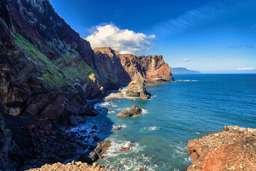 The picture showcases a picturesque rocky coastline with a dominant, tall rock rising from the azure waters of the ocean, under a clear sky. It's a scene full of tranquility and the majesty of nature.