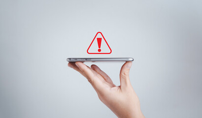 Hand holding smartphone with red triangle caution warning sign for notification error and maintenance concept.