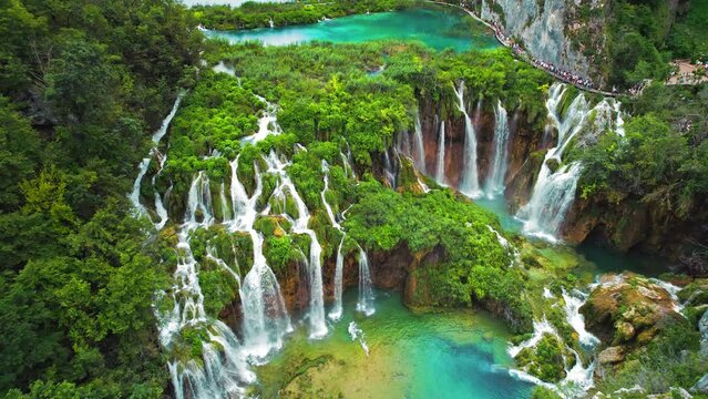 Crowd of tourists visit famous Plitvice waterfalls in Croatia. Summer landscape. Mountain streams flow into a lake with azure clear water.