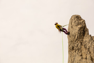A man is climbing a rock wall with a green rope. Concept of adventure and excitement, as the man is...